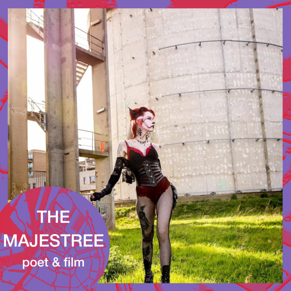The Majestree, poet & film, poses against an industrial backdrop with silos and grass.