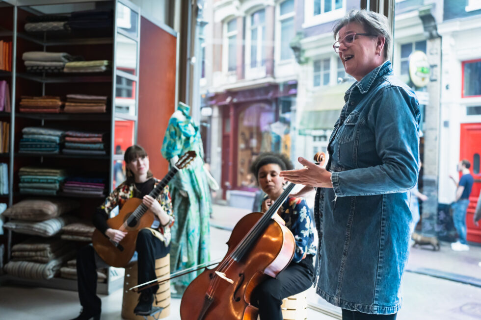 Live music performance in a shop: guitarist, cellist, and speaker.