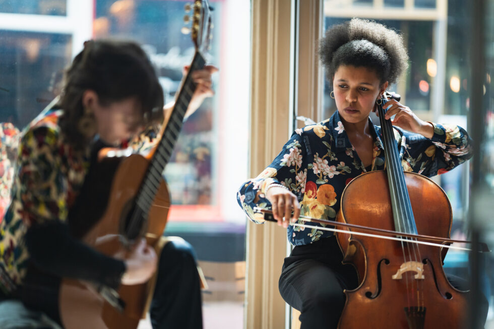 Two musicians performing: a woman playing cello and a person playing acoustic guitar.