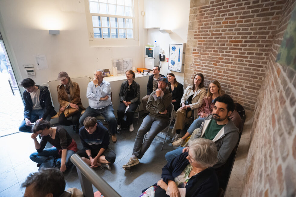 Group of people attentively listening in an indoor performance setting with brick wall and window.