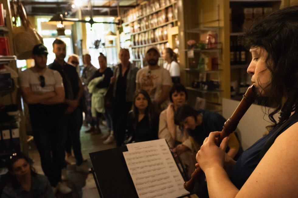 Musician playing recorder for an audience in a bookstore, sheet music on stand.