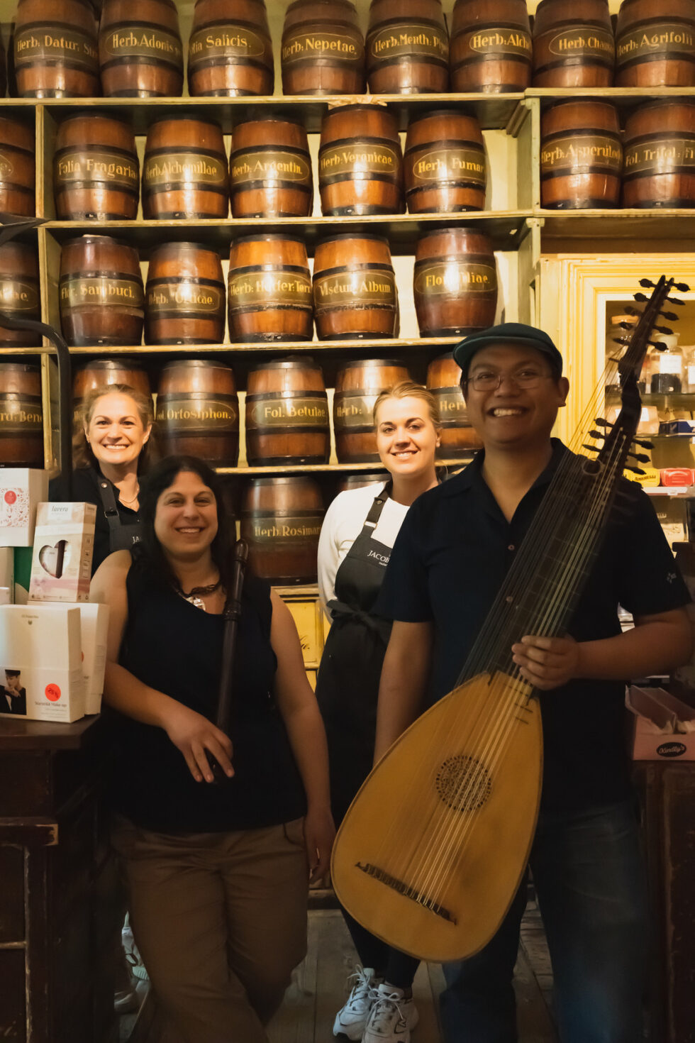 Group in a vintage apothecary with a lute player and recorder player - barrels in background labeled with herbs.