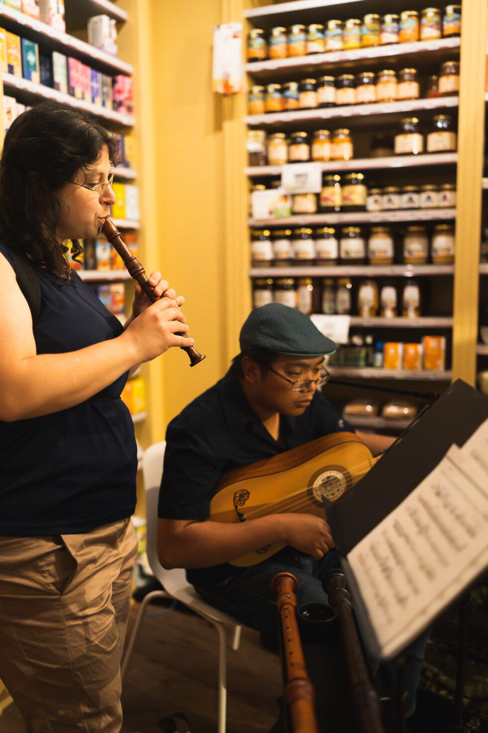 Musicians playing recorder and lute in a shop with shelves of jars.