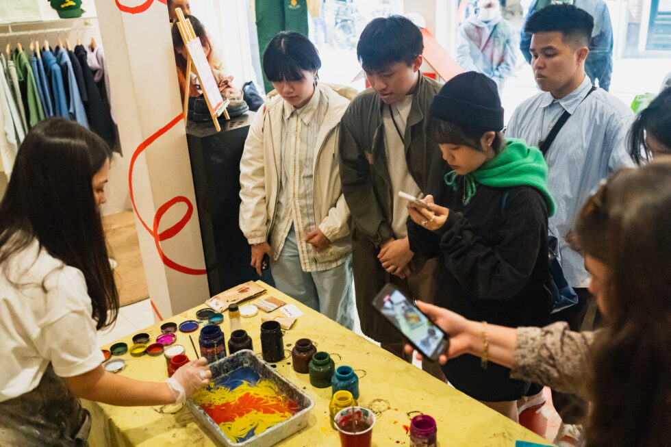 People around a table with paint, one person taking a video of the process using a phone