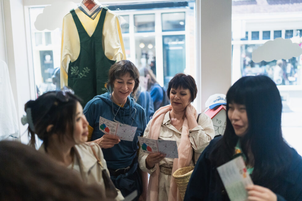 Four women holding Pop-In Day flyers in clothing in a store