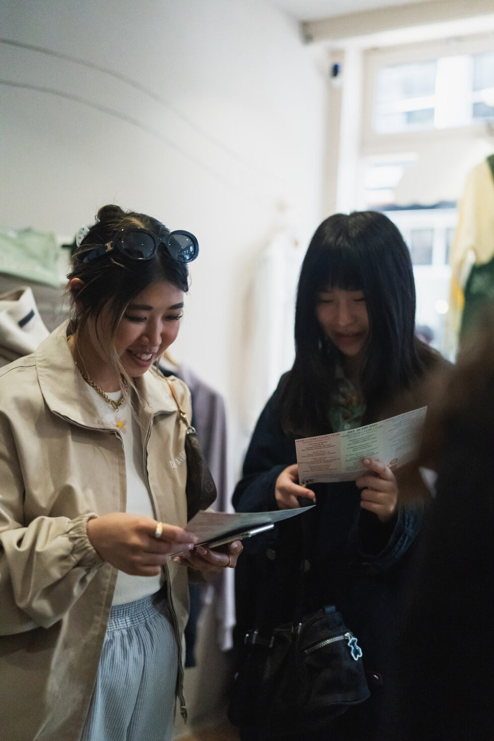 Two women smiling, reviewing the Pop-In Day poster map in a clothing store.