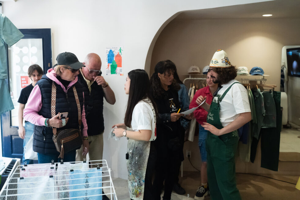 People in a clothing store, some looking at a rack with artwork. Person talking to the artist. Pop-In Day poster in background.
