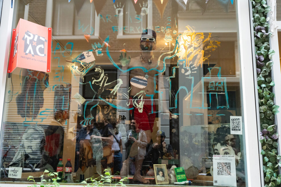 Art installation in a window with a shirtless man, signs, and reflections.