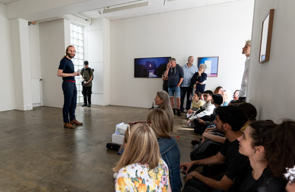Presentation in an art gallery with attendees seated and standing.