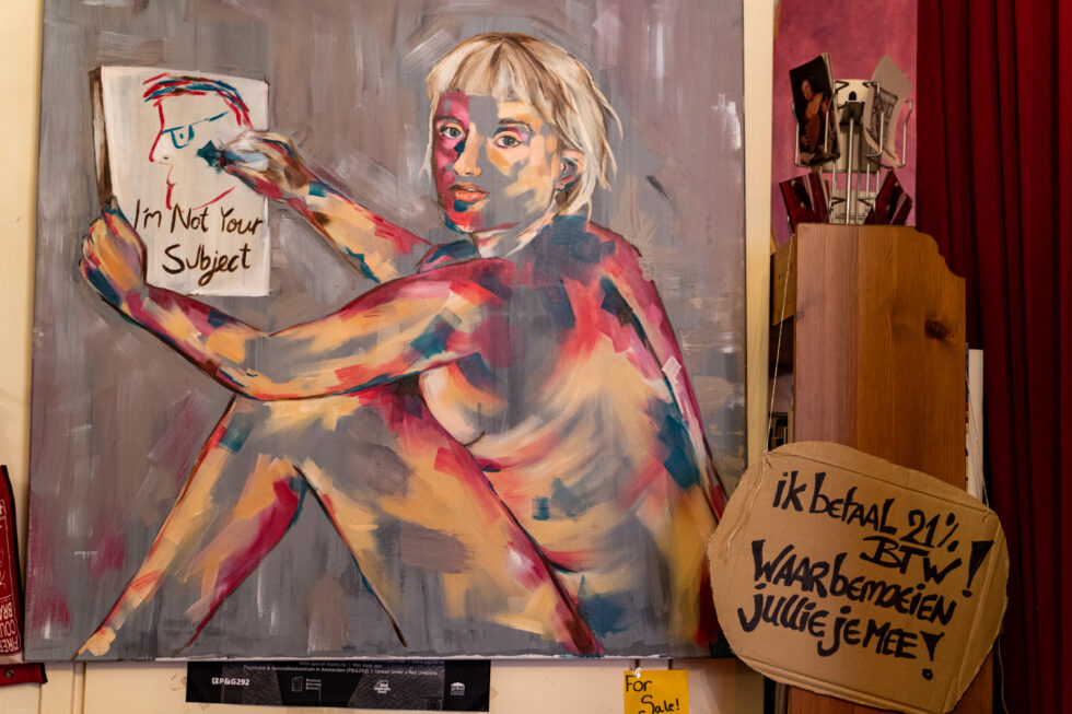 Painting of a nude woman holding a sign reading 