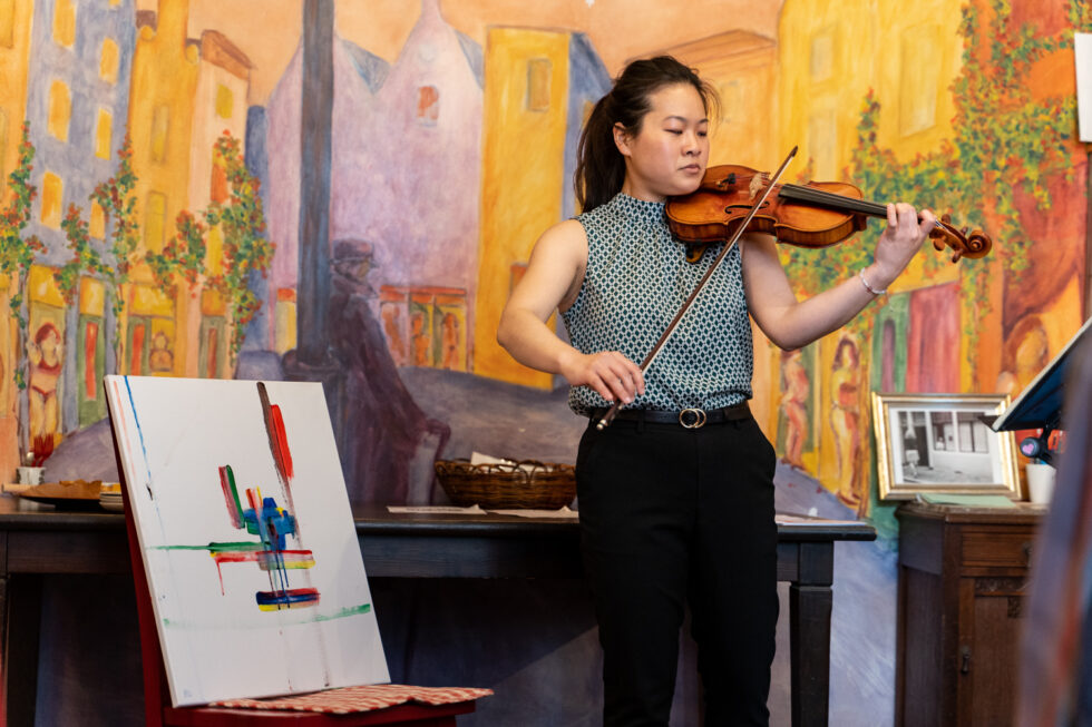 Woman playing violin in front of colorful mural art.
