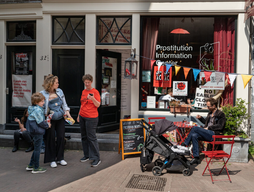 Family outside Amsterdam's Prostitution Information Center, featuring posters and educational materials about sex work.