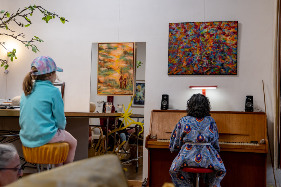 Woman in patterned dress playing piano in a room with paintings