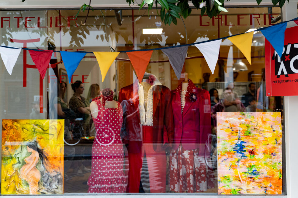 Colorful atelier gallery window display with clothing and art.