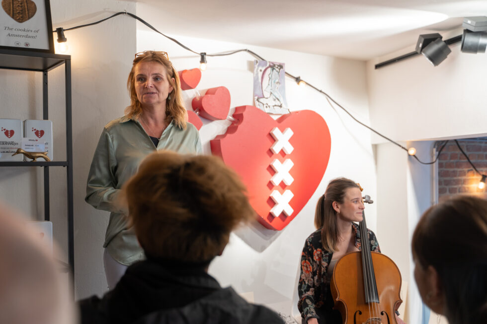 Woman speaking next to a cellist with an Amsterdam heart in the background
