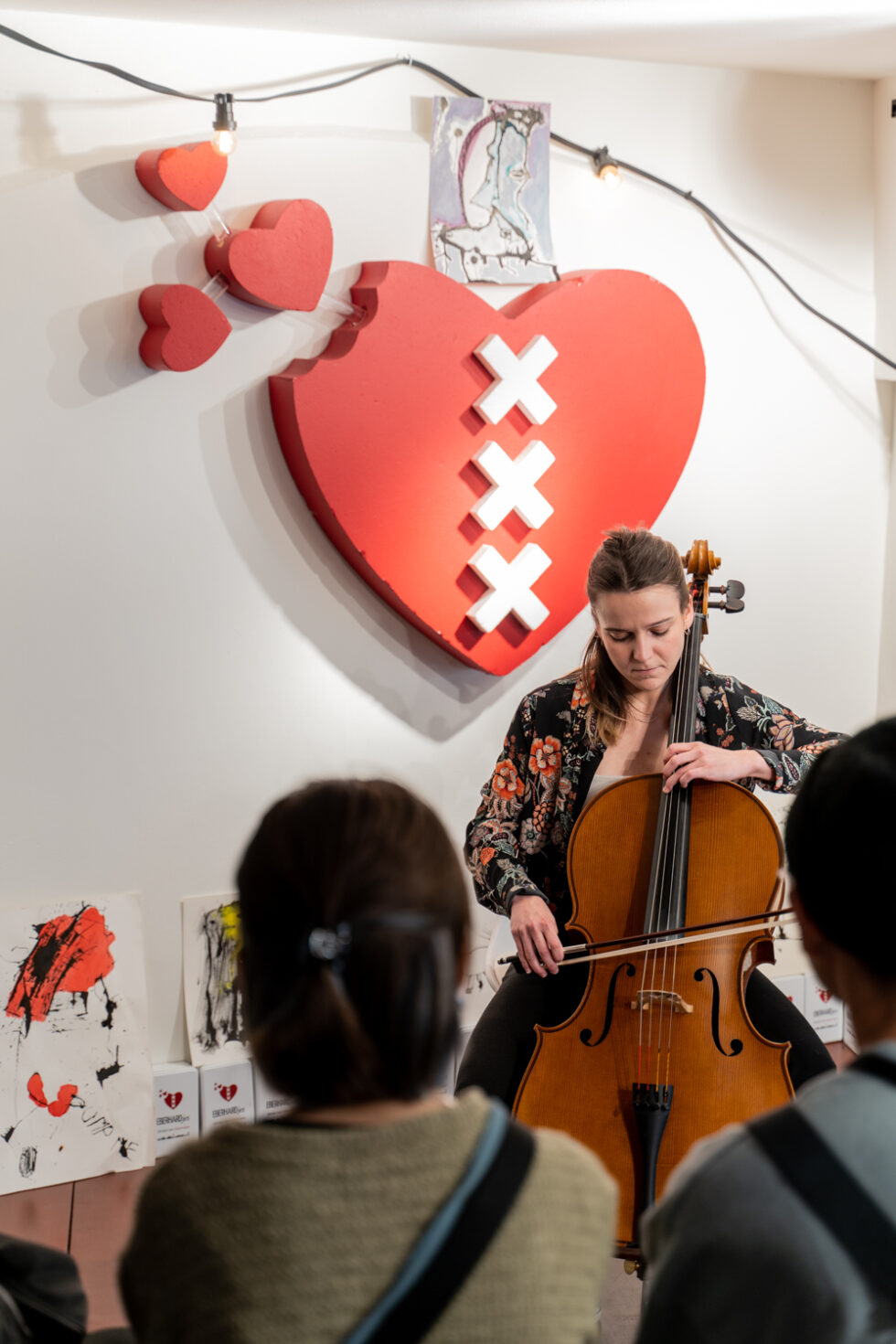 Cellist performing in front of Amsterdam heart art.