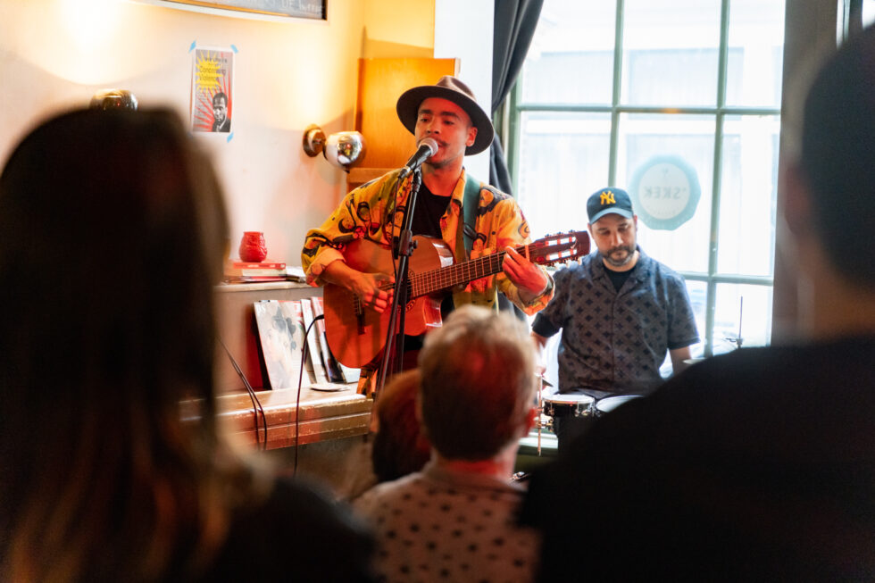 Live music performance: Musician with guitar and drummer playing in a bar.