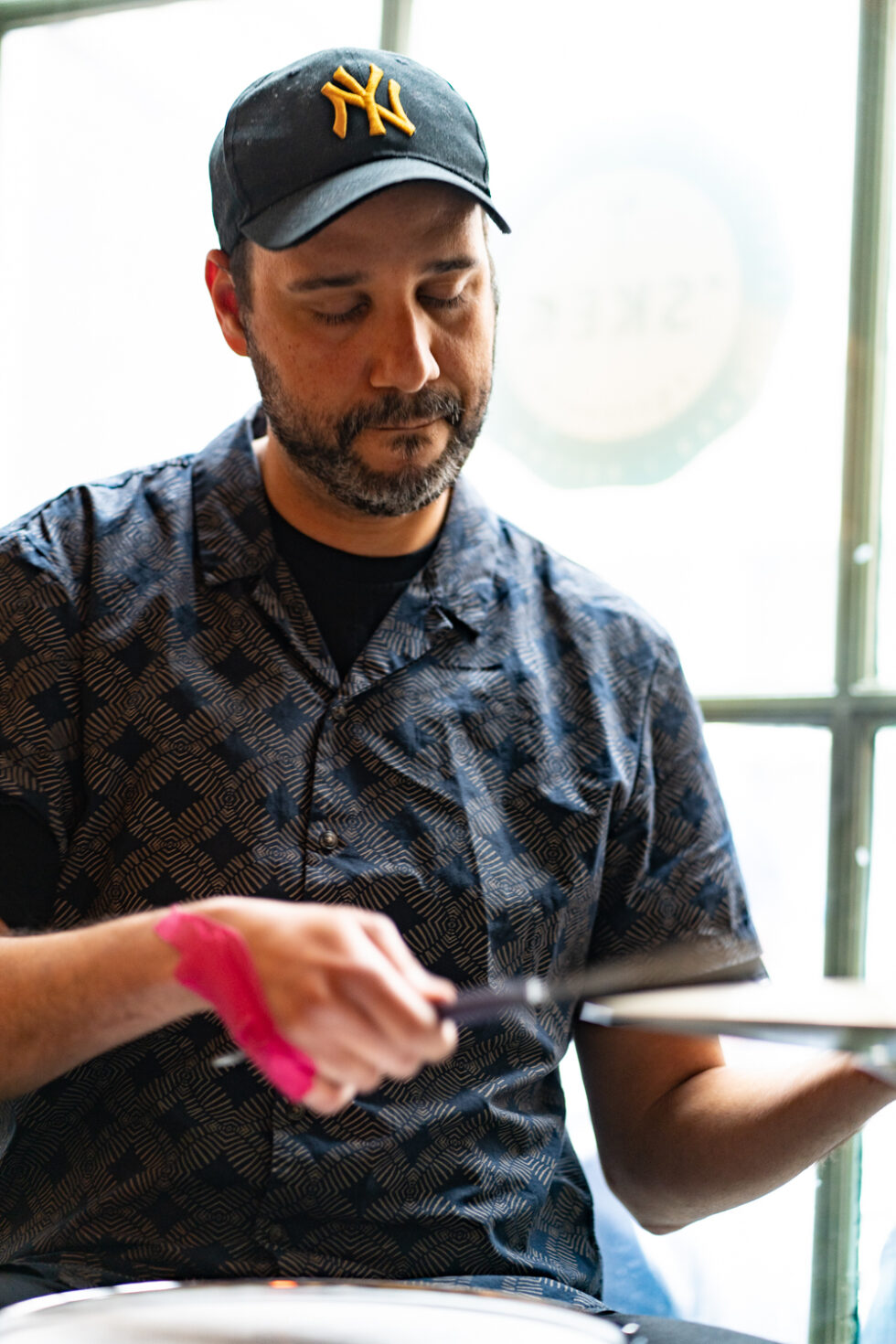 Drummer with NY cap playing cymbals, pink tape on wrist