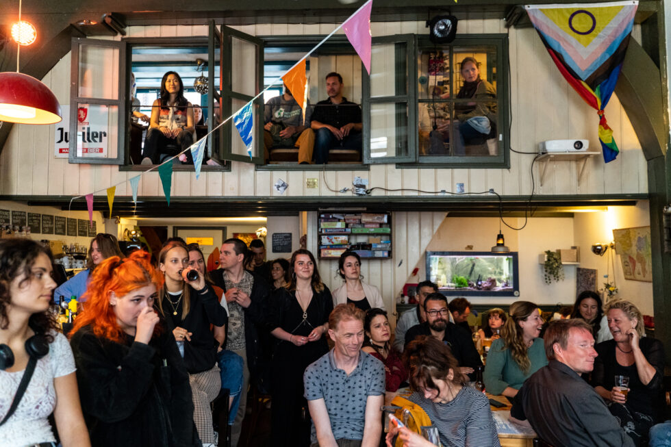 Crowded bar scene with people watching from windows above, colorful bunting and flags
