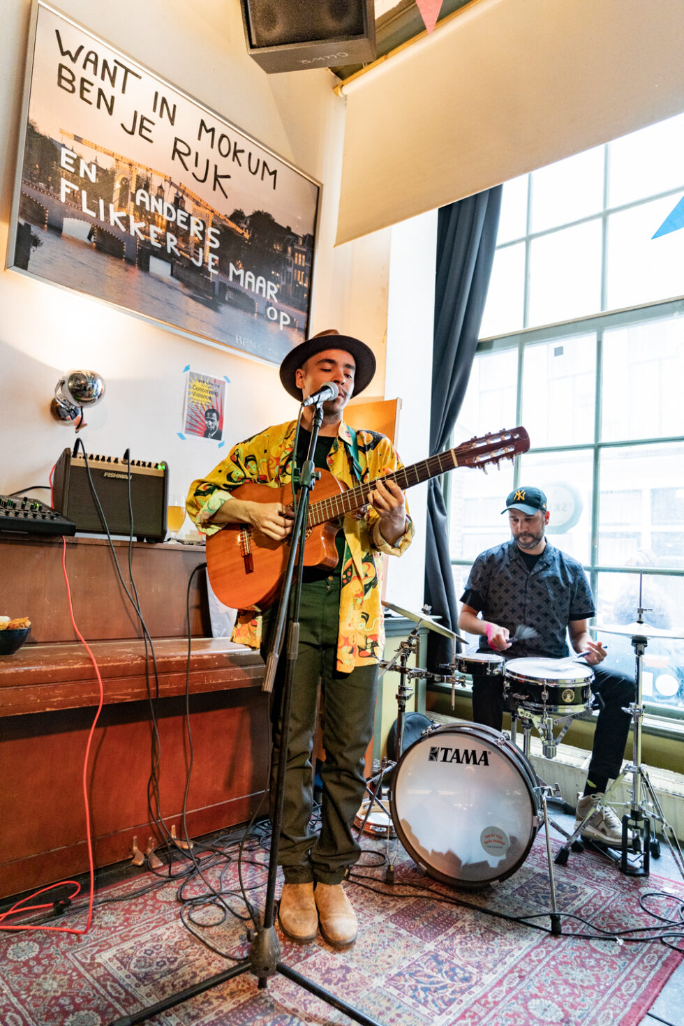 Live music performance: Musician playing guitar, drummer behind. 