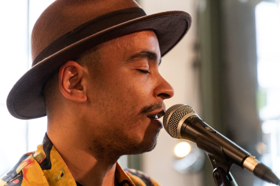 Man with hat singing into a microphone, eyes closed in performance.